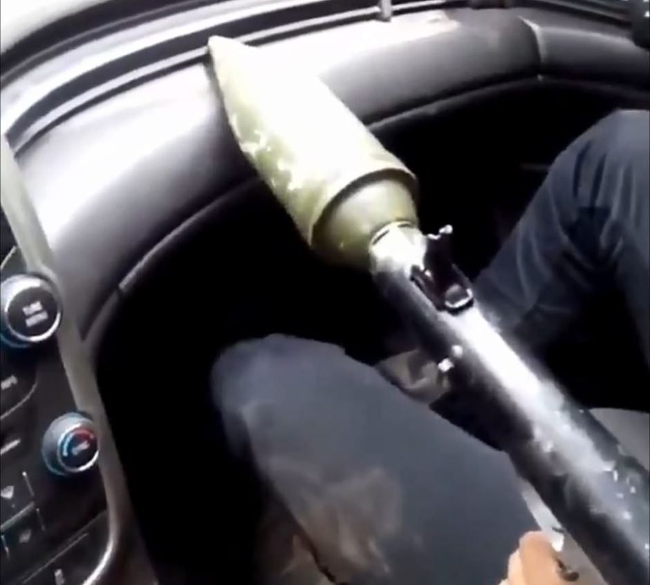 A cartel member holds a grenade launcher in a car