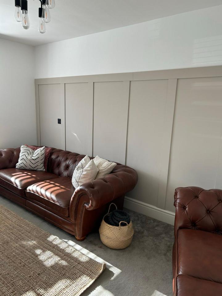 Brown leather chesterfield sofa and armchair in front of a beige paneled wall.