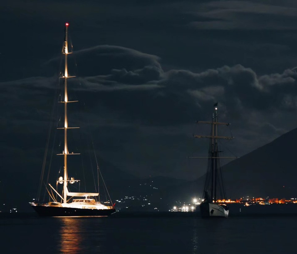two sailboats are in the water at night with mountains in the background
