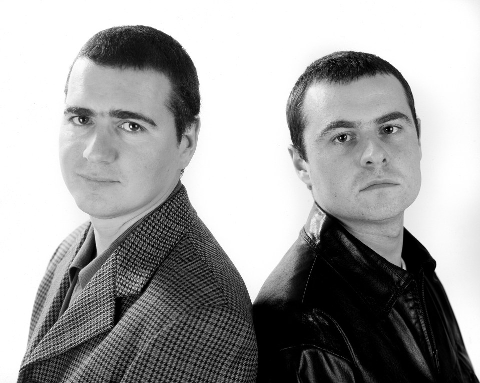 two men are standing back to back and looking at the camera