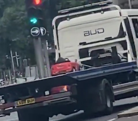 a bud truck is driving down a street next to a red light .