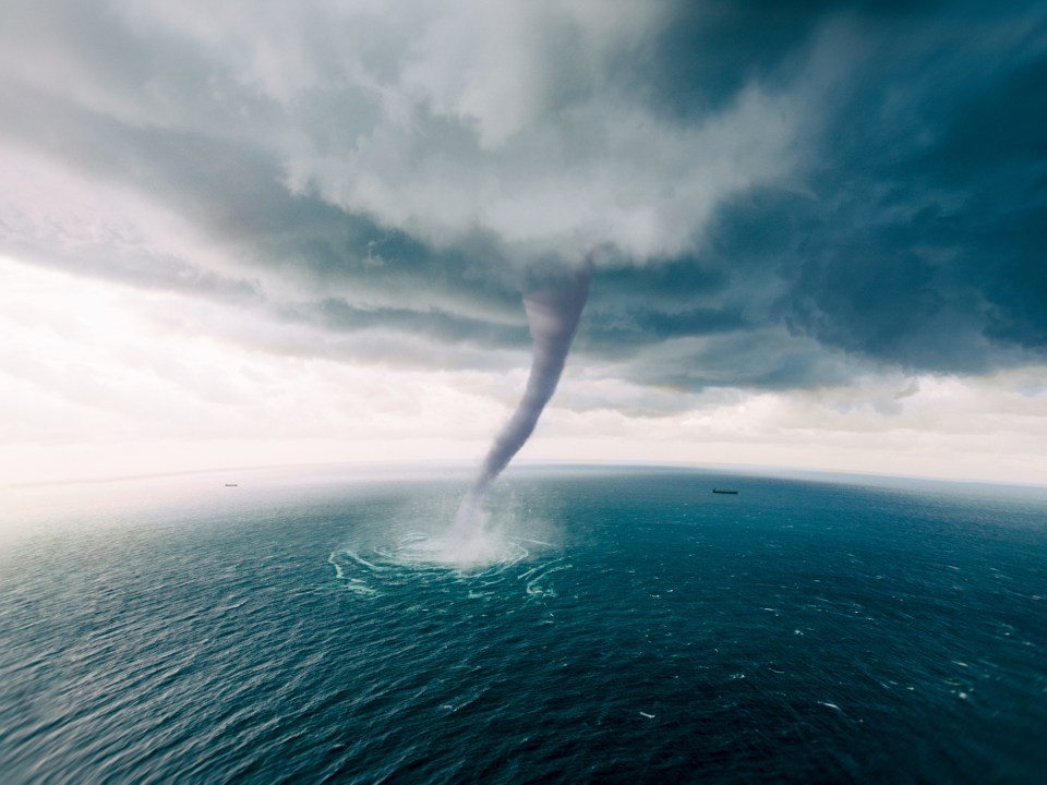 a tornado in the middle of the ocean with a boat in the distance
