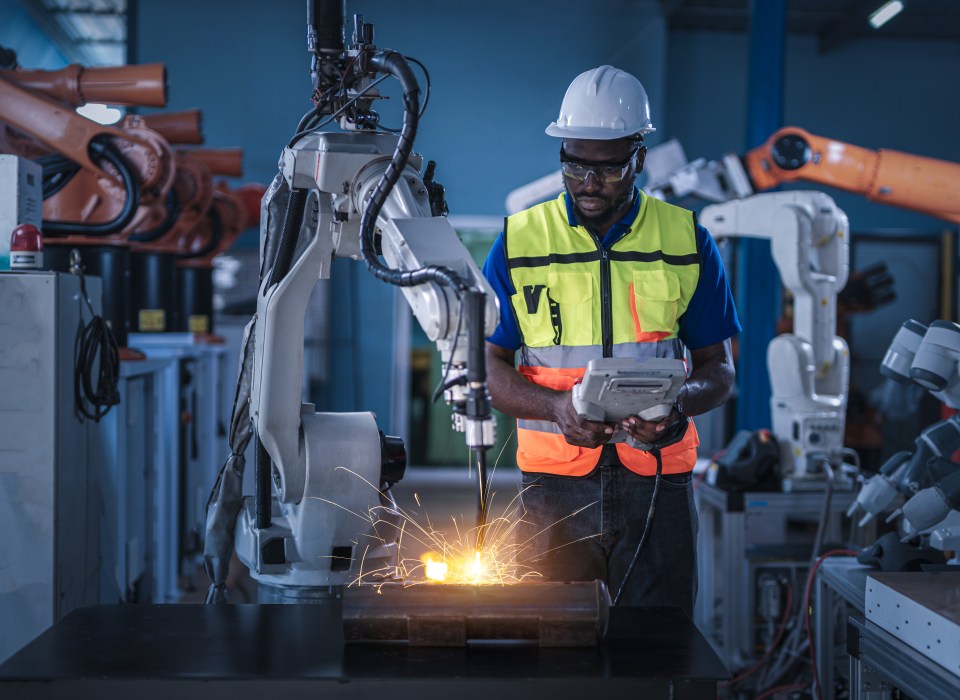 a man wearing a hard hat and safety vest is working on a robotic arm