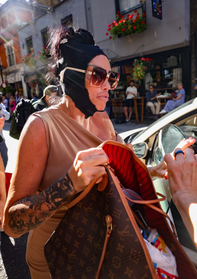 a woman wearing a black mask and sunglasses holds a louis vuitton bag