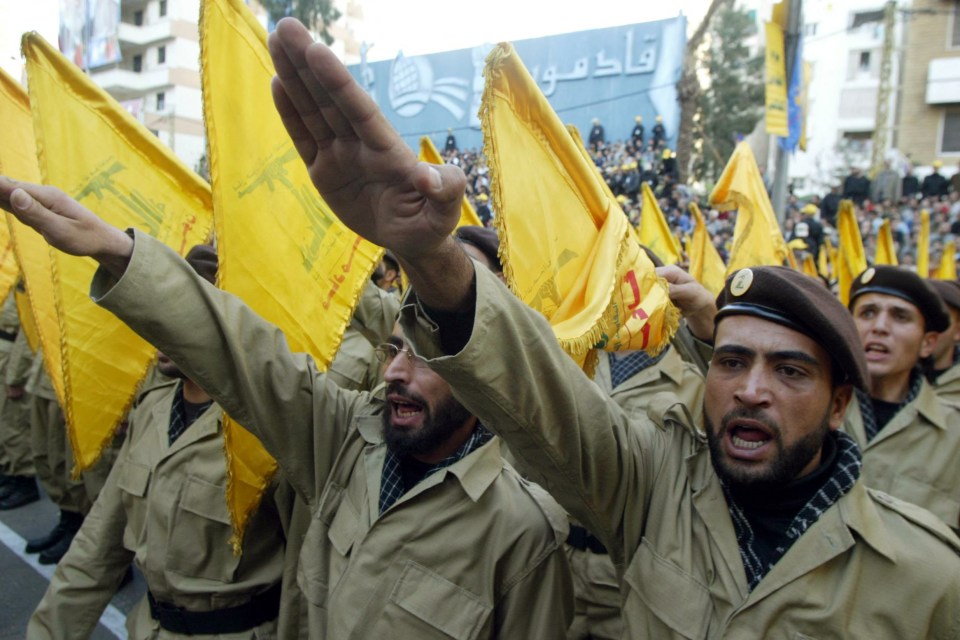 a group of men in khaki uniforms holding yellow flags with arabic writing on them
