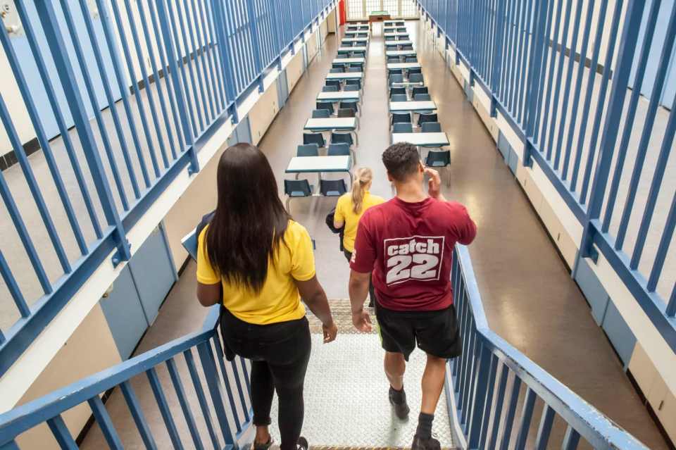 a man wearing a catch 22 shirt walks down stairs