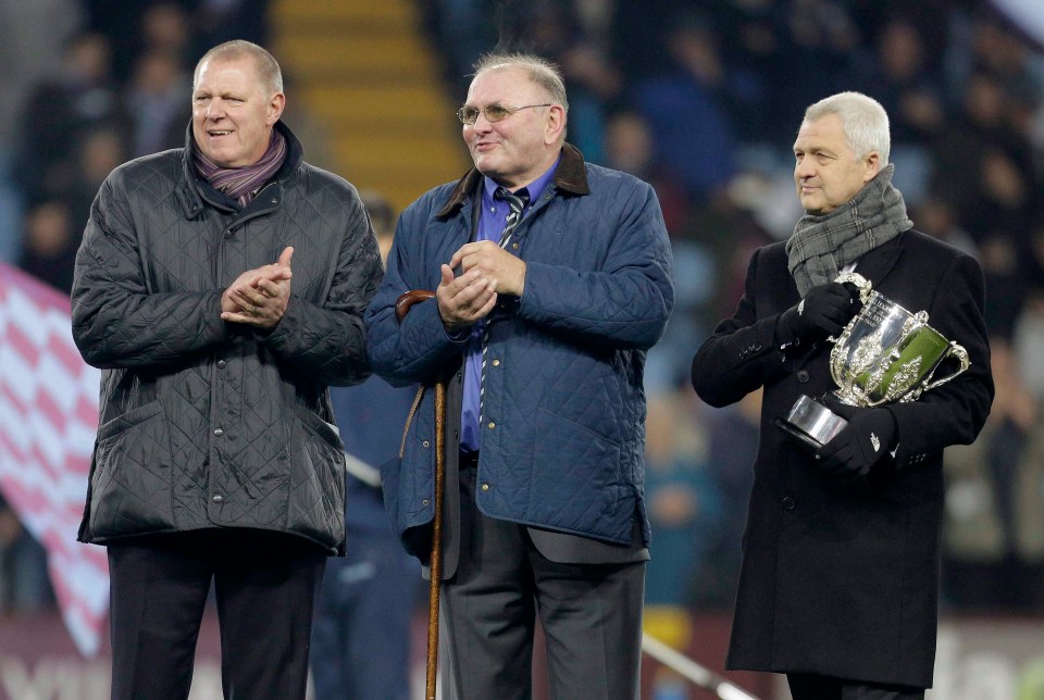 three men stand on a field with one holding a trophy