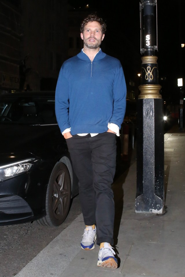 a man in a blue sweater stands in front of a black car