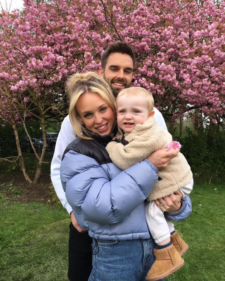 a man and woman holding a baby in front of a tree with pink flowers