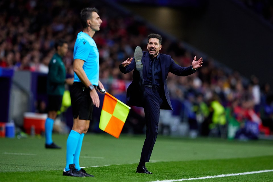 a man in a suit kicks a yellow and orange flag on a soccer field
