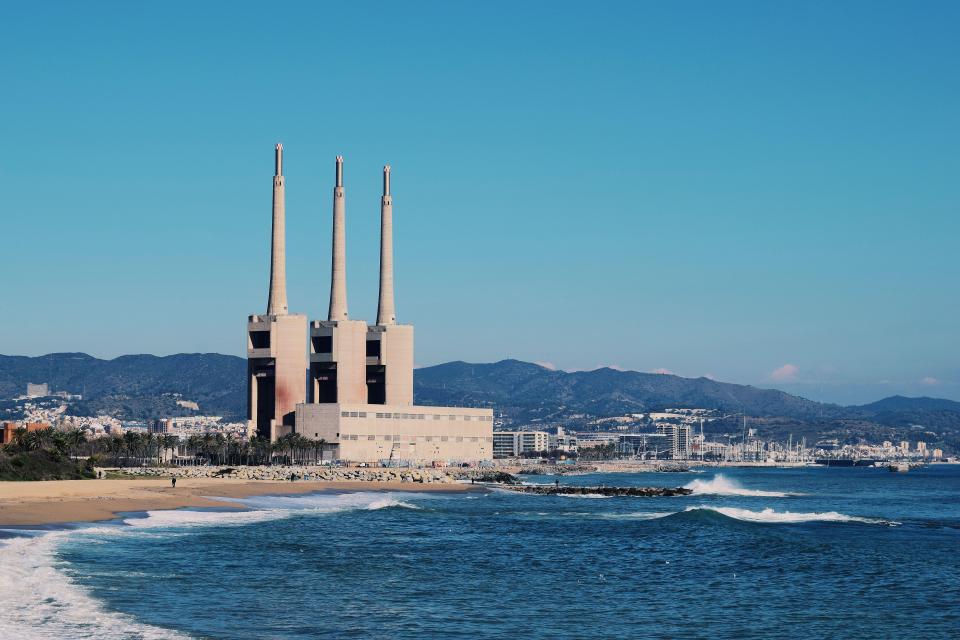 a large building with three chimneys sits on the shore of the ocean