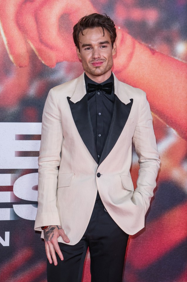 a man in a tuxedo stands on a red carpet with his hands in his pockets