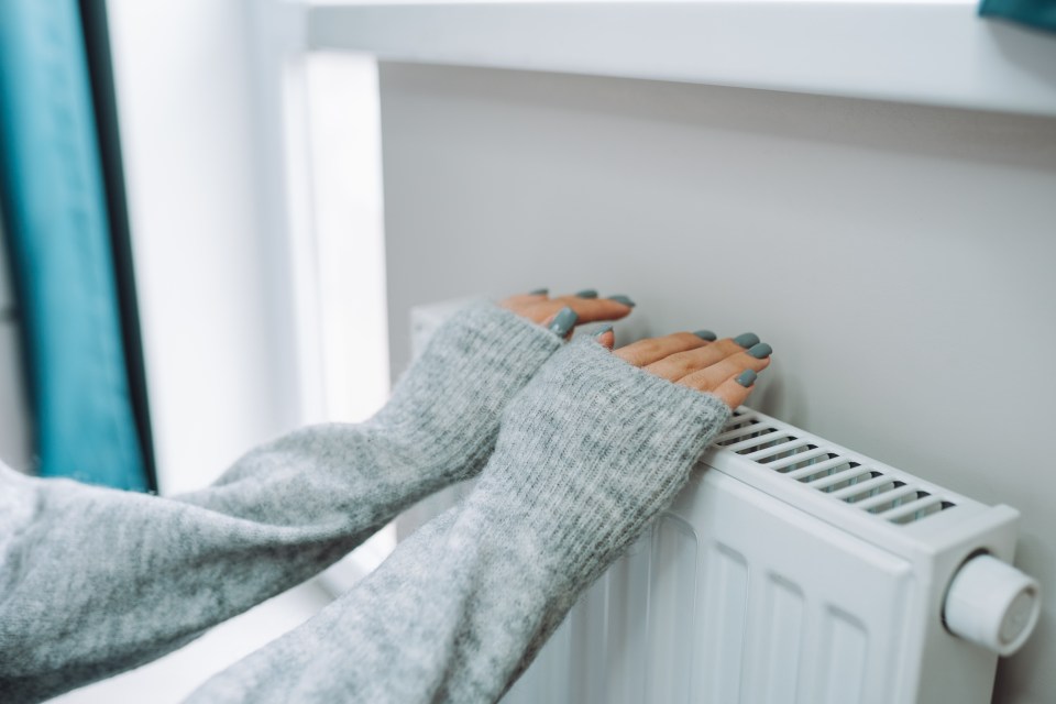 a woman in a grey sweater is touching a radiator