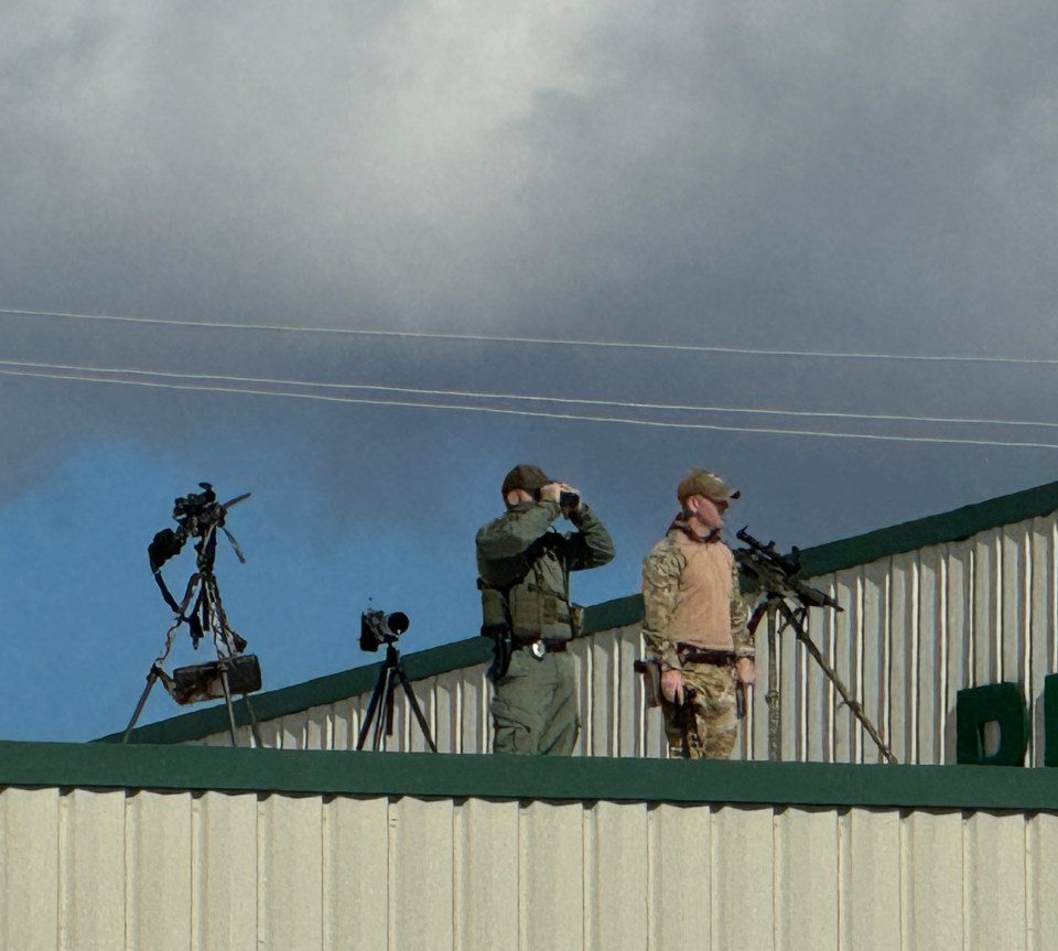 two men standing on top of a building looking through binoculars