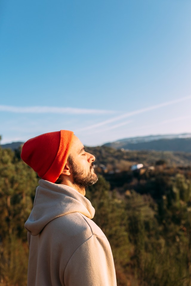 a man wearing a red beanie and a hoodie looks up at the sky