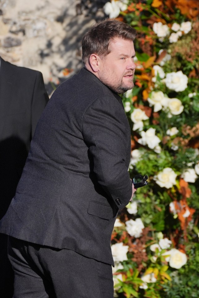 a man in a suit stands in front of flowers