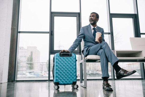 a man in a suit sits on a chair with a blue suitcase