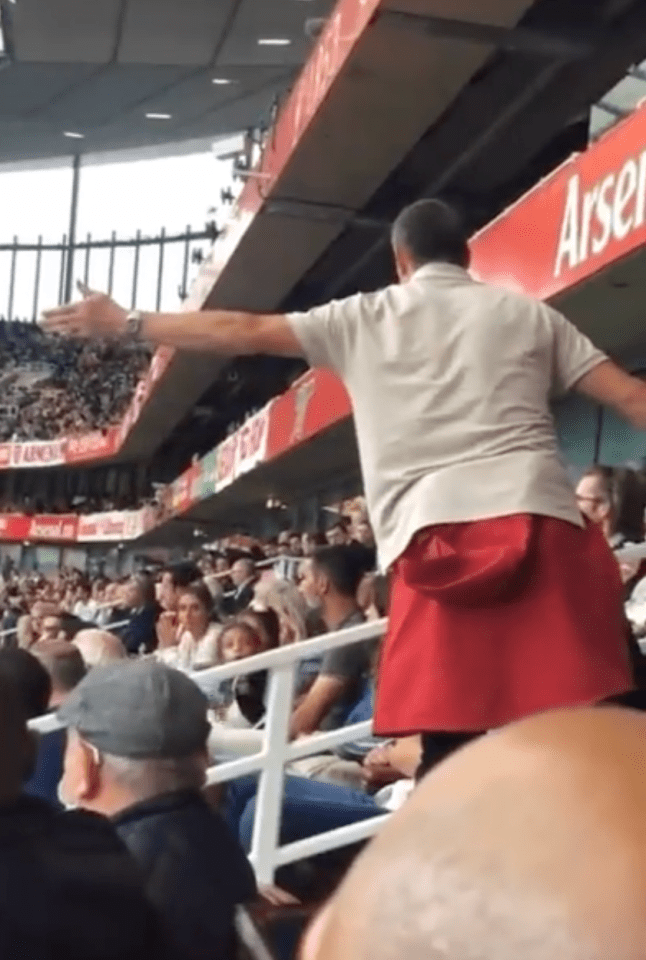 a man in a red skirt stands in front of a sign that says arsenal