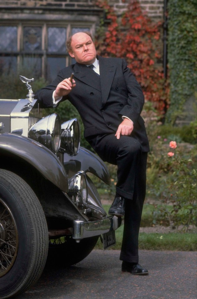 a man in a suit leans on a rolls royce car