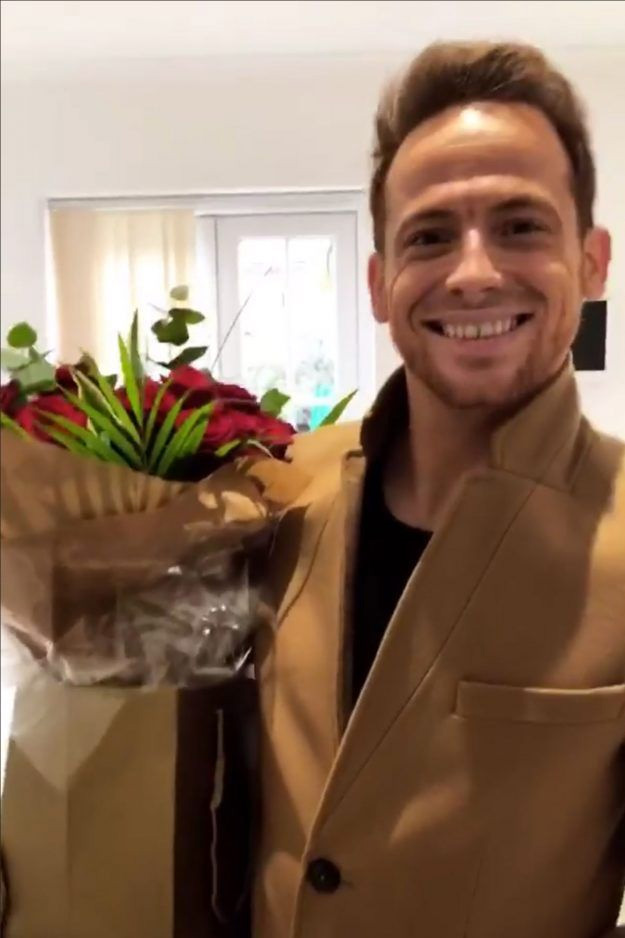 a man in a tan coat is smiling while holding a box of flowers