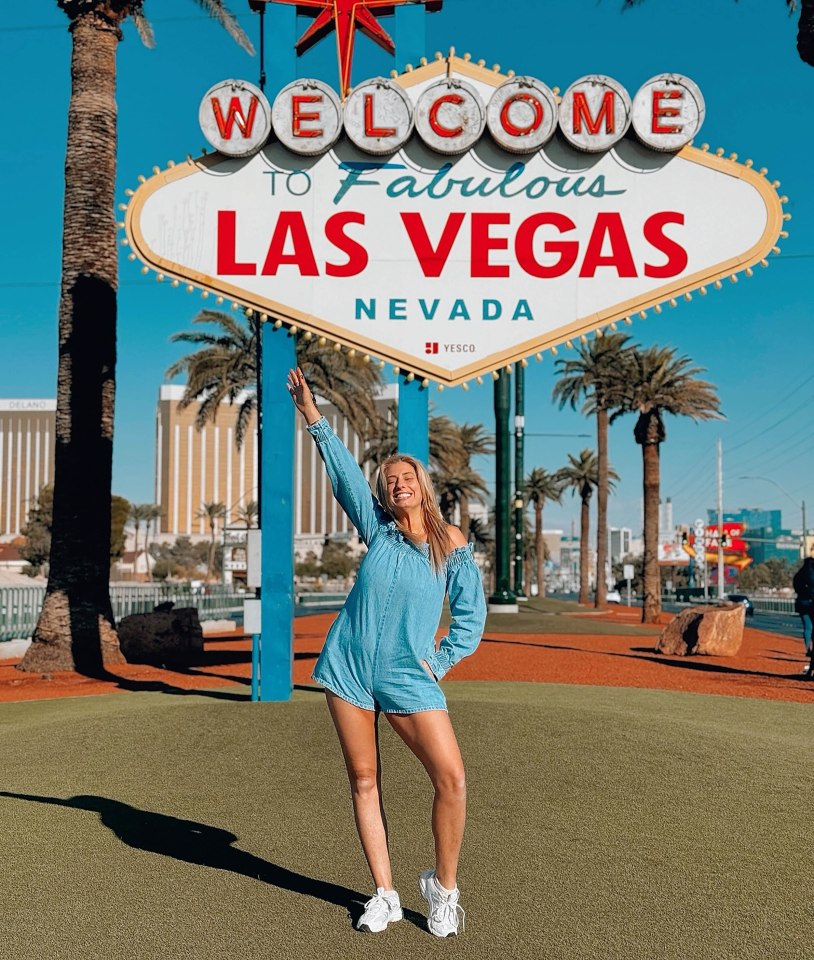 a woman stands in front of a welcome to fabulous las vegas sign