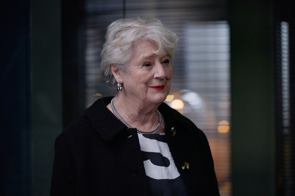 an older woman wearing a black coat and a pearl necklace