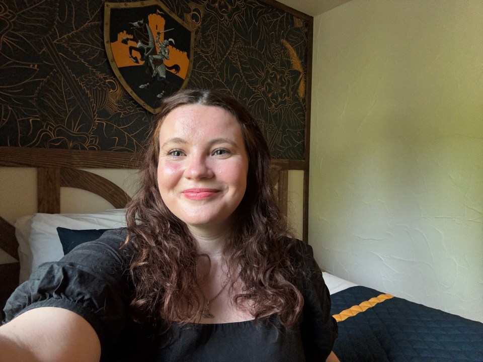 Woman smiling for a selfie in a bedroom with a medieval-themed headboard.