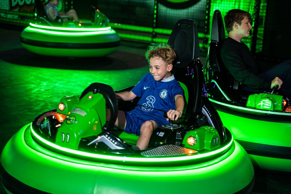 Boy driving a green bumper car at an indoor adventure park.