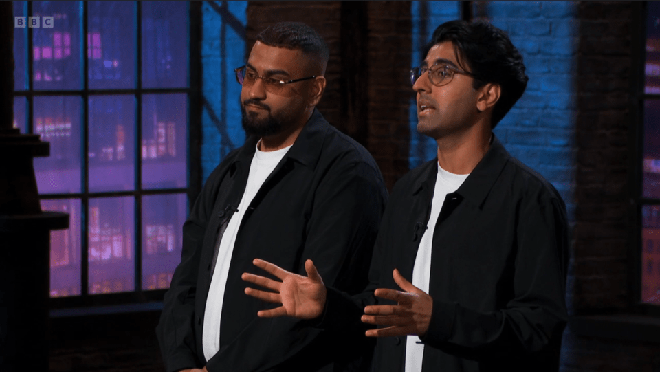 Two men in black jackets and glasses talking.