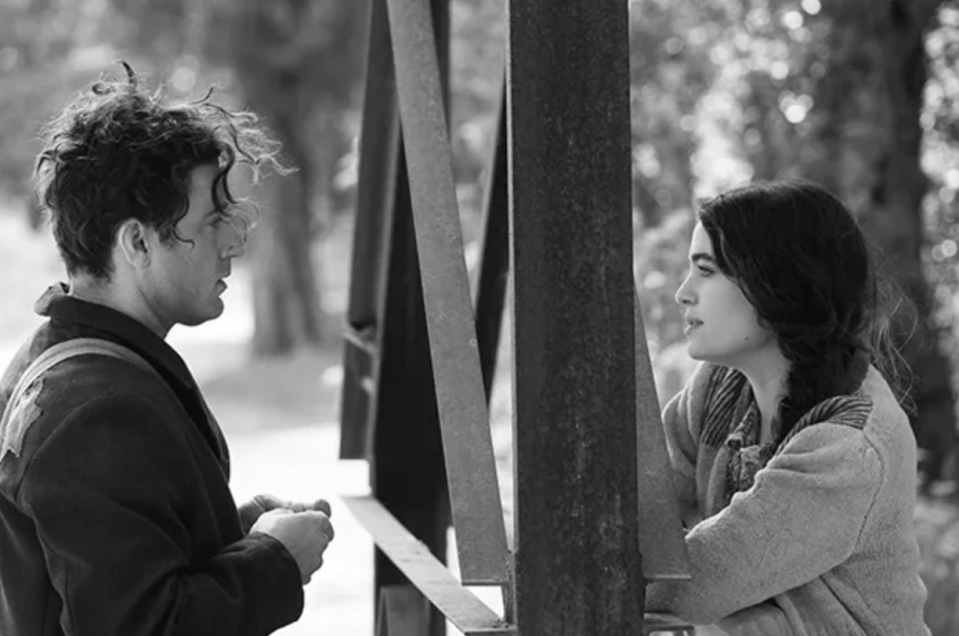 Black and white photo of a man and woman talking, separated by a metal structure.