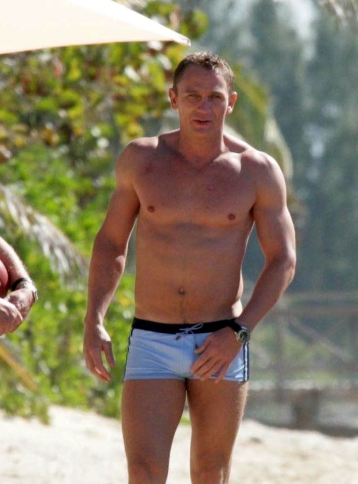 Daniel Craig on a beach in swim trunks.