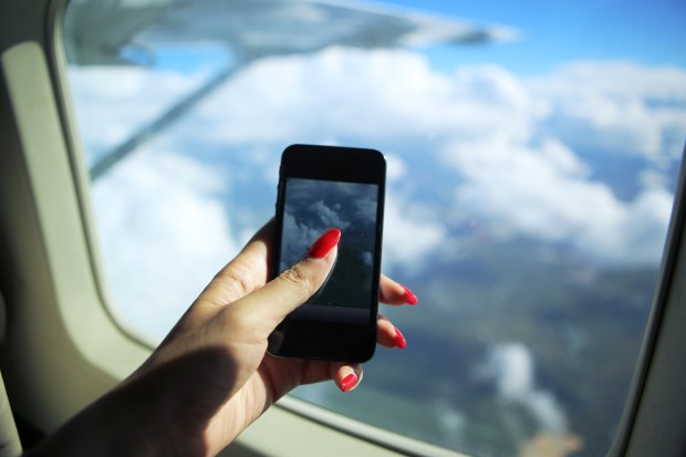 Woman taking a picture of clouds from airplane window using smartphone.