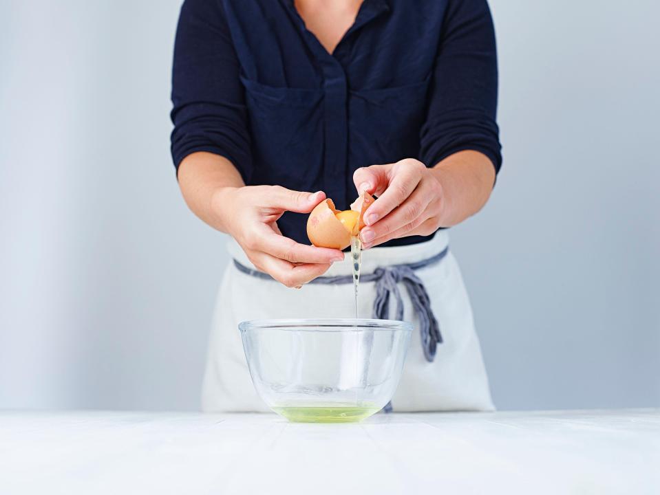 Person separating an egg yolk into a glass bowl.