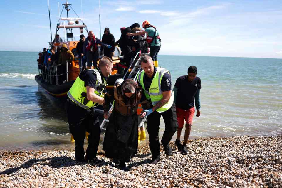 Migrants arriving by boat are helped ashore by officers.