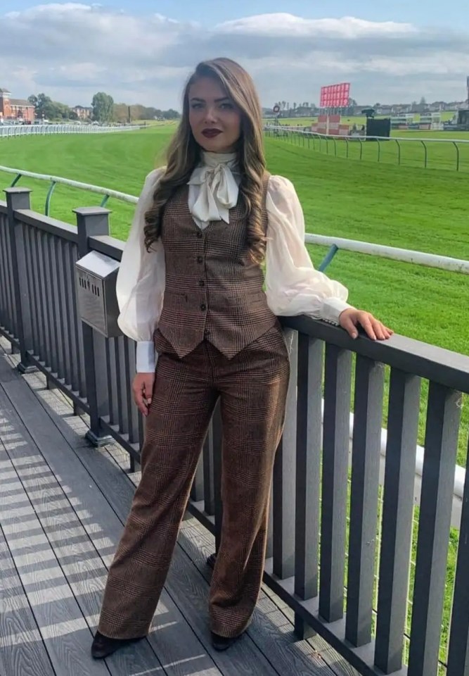Woman in brown pantsuit at a racetrack.