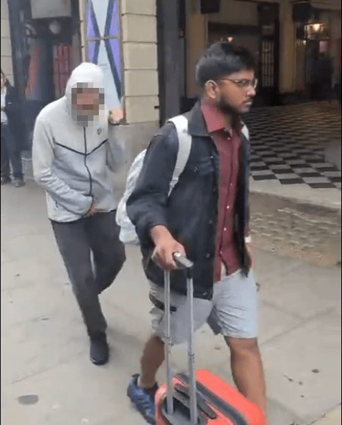 Two men walking down a city street, one pulling a suitcase.