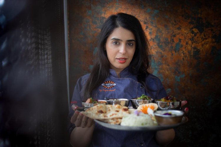 A woman chef holding a platter of Indian food.