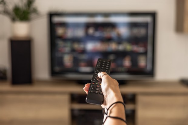 Woman's hand holding a smart TV remote, with a streaming service screen in the background.