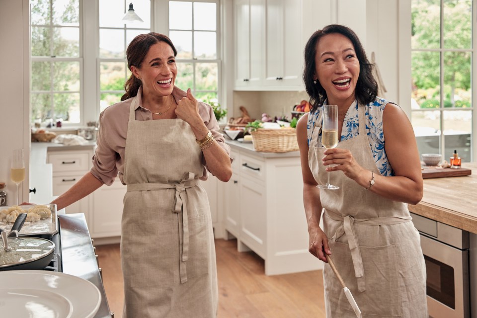 Meghan Markle and Vicky Tsai laughing together in a kitchen while cooking.
