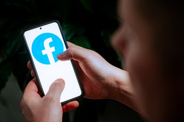 Photo illustration of a person using a smartphone displaying the Facebook logo.