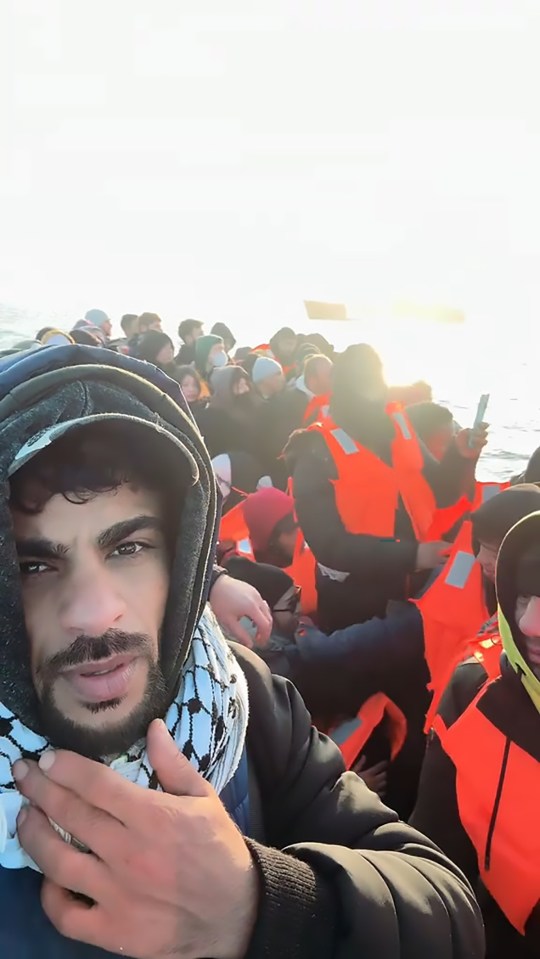 A man in an orange life vest on a crowded migrant boat.