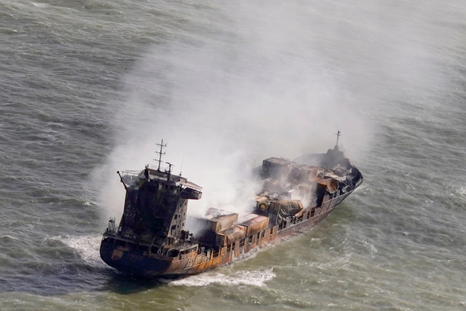 Aerial view of a burning cargo ship in the North Sea, with a tugboat nearby.