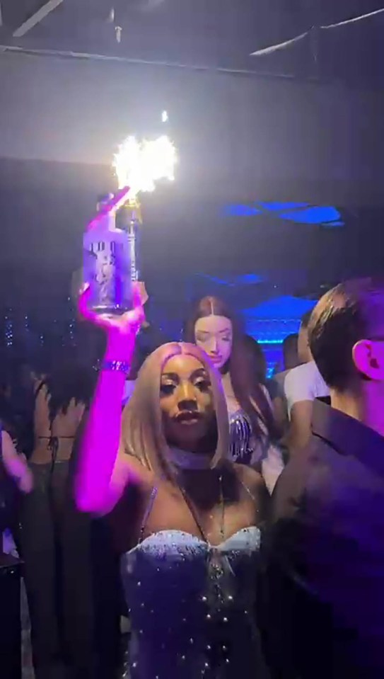 Person holding a bottle with sparklers in a nightclub.