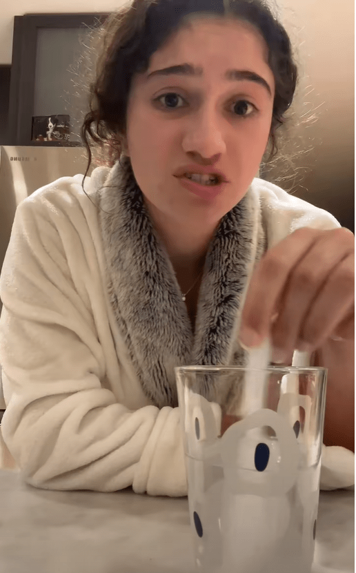 Woman in bathrobe adding something to a glass of water.