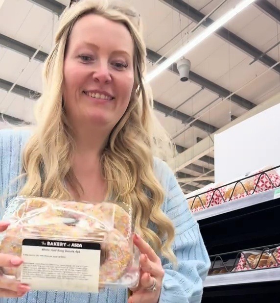 Woman in a supermarket holding a package of ring donuts.