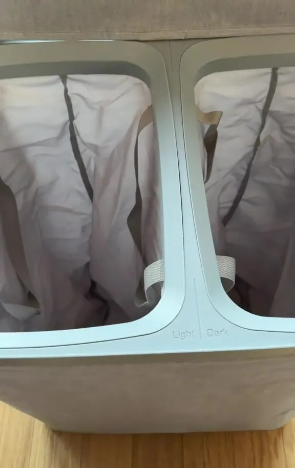 Double laundry hamper with light and dark compartments.