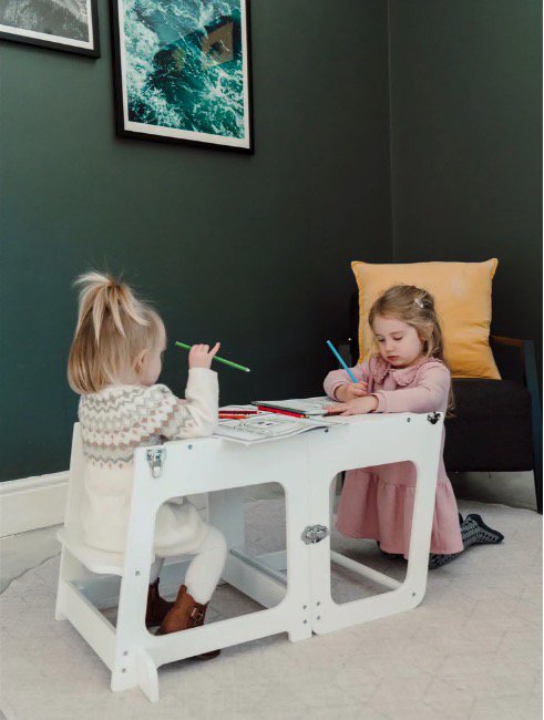 Two toddlers sitting at a white children's learning tower drawing.