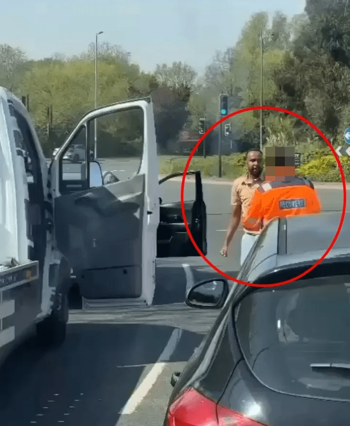Video still of a road rage incident: a man in a beige shirt punches a recovery truck driver in an orange jacket.