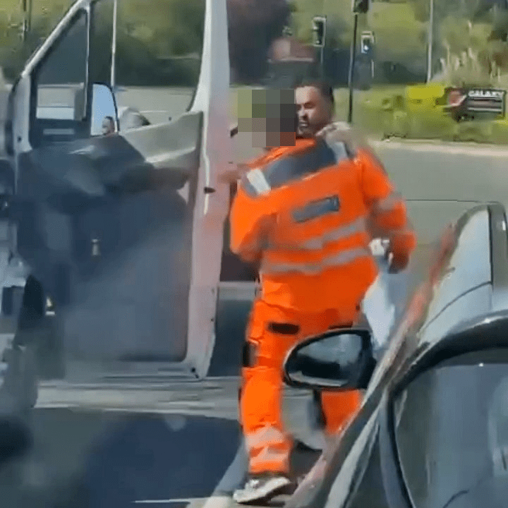 A road rage incident where a driver in a beige shirt punches a recovery truck driver in an orange hi-viz jacket.