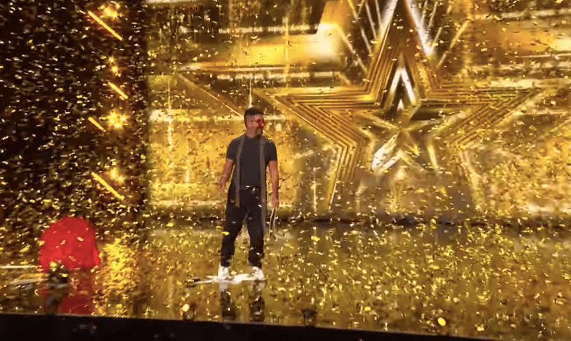 Man standing on stage covered in gold confetti.
